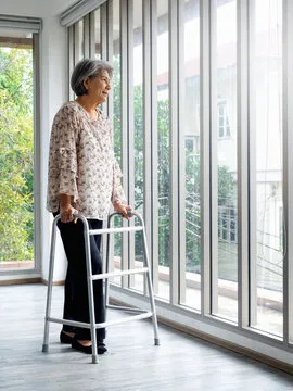 Asiatische Seniorin mit weißen Haaren steht mit Gehhilfe von Ostewind Betreuungs- und Entlastungsdienst